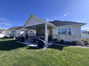 Back of property featuring stone siding, a patio area, and a shingled roof