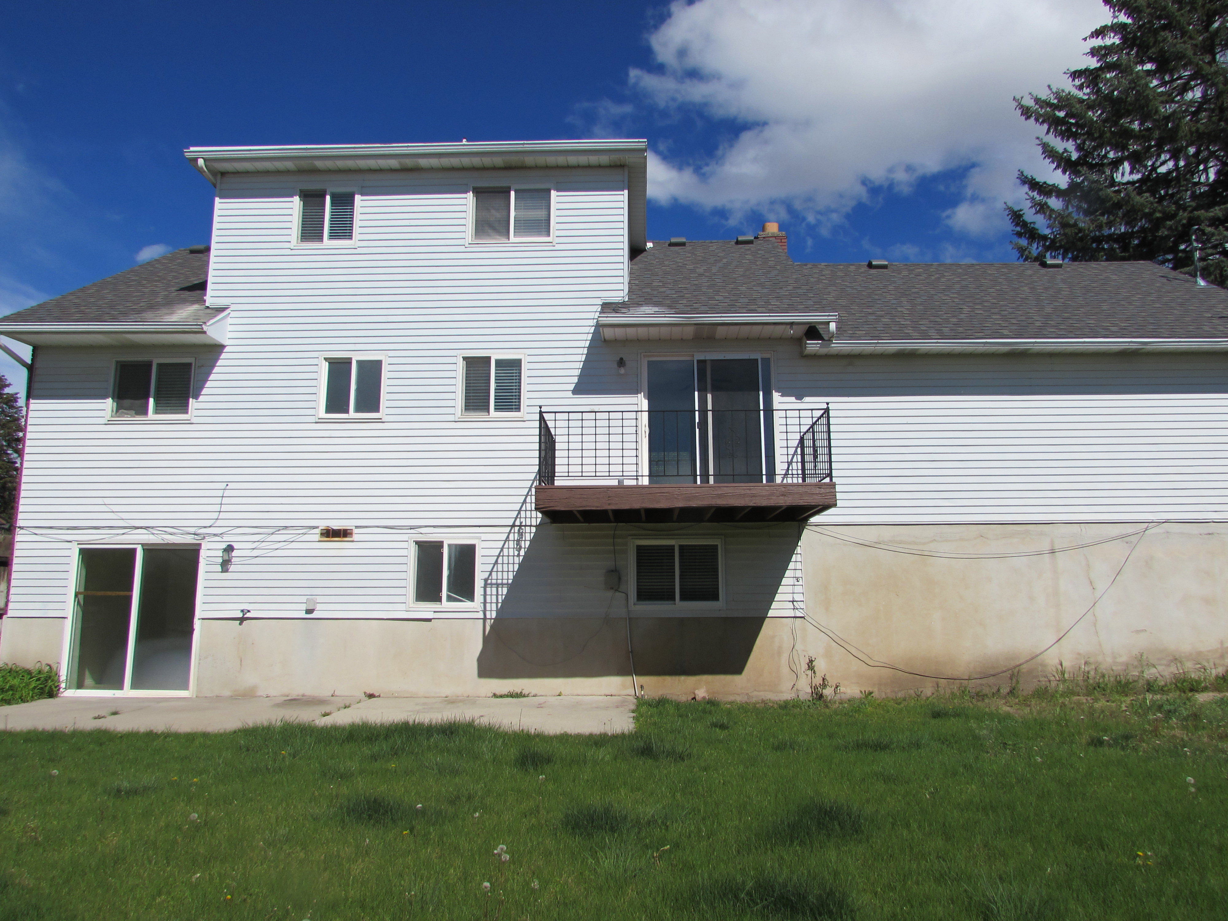 Back of property featuring a patio, balcony, a shingled roof, a lawn, and a chimney