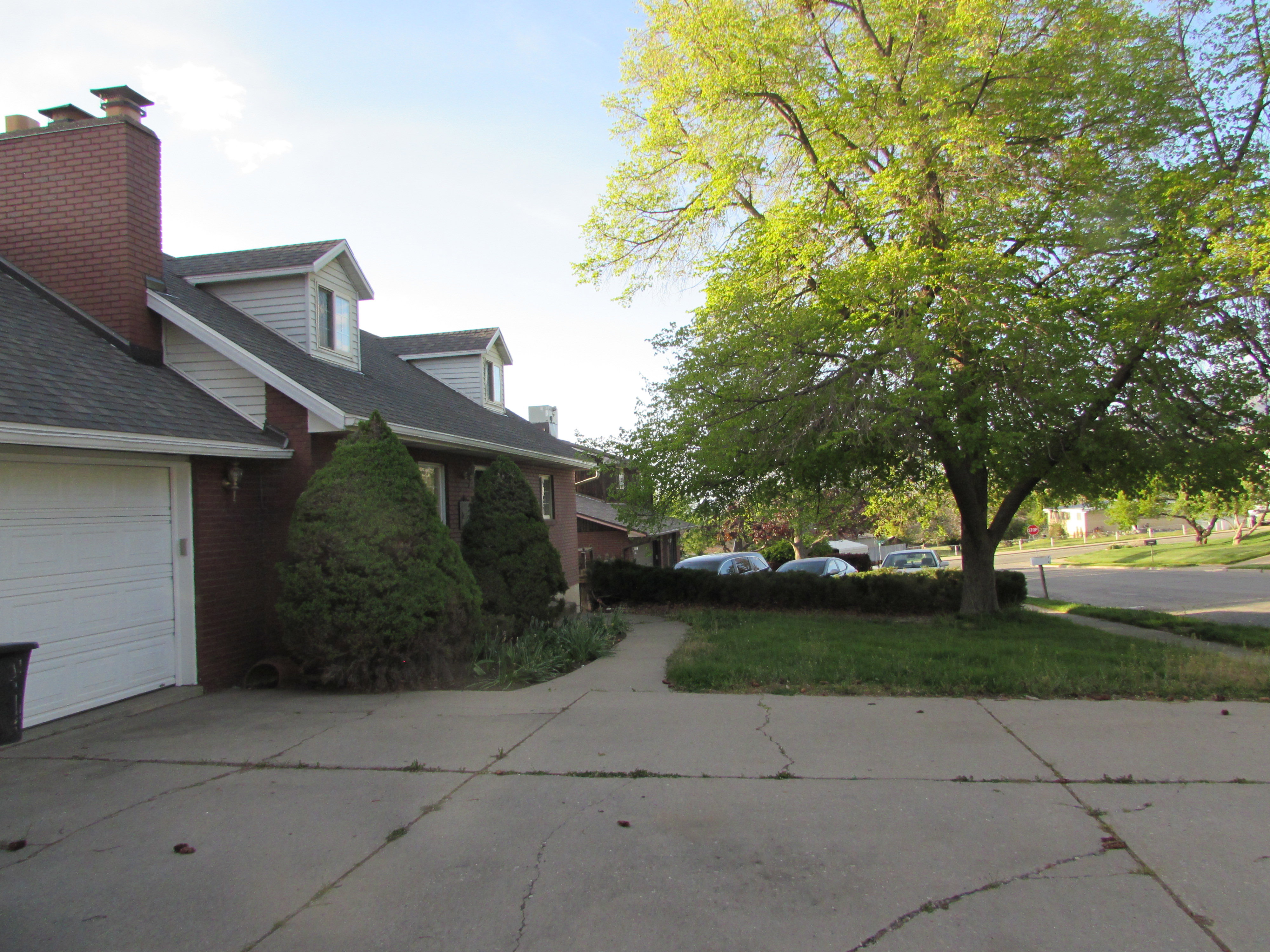 View of side of property with brick siding, a shingled roof, driveway, a lawn, and a garage
