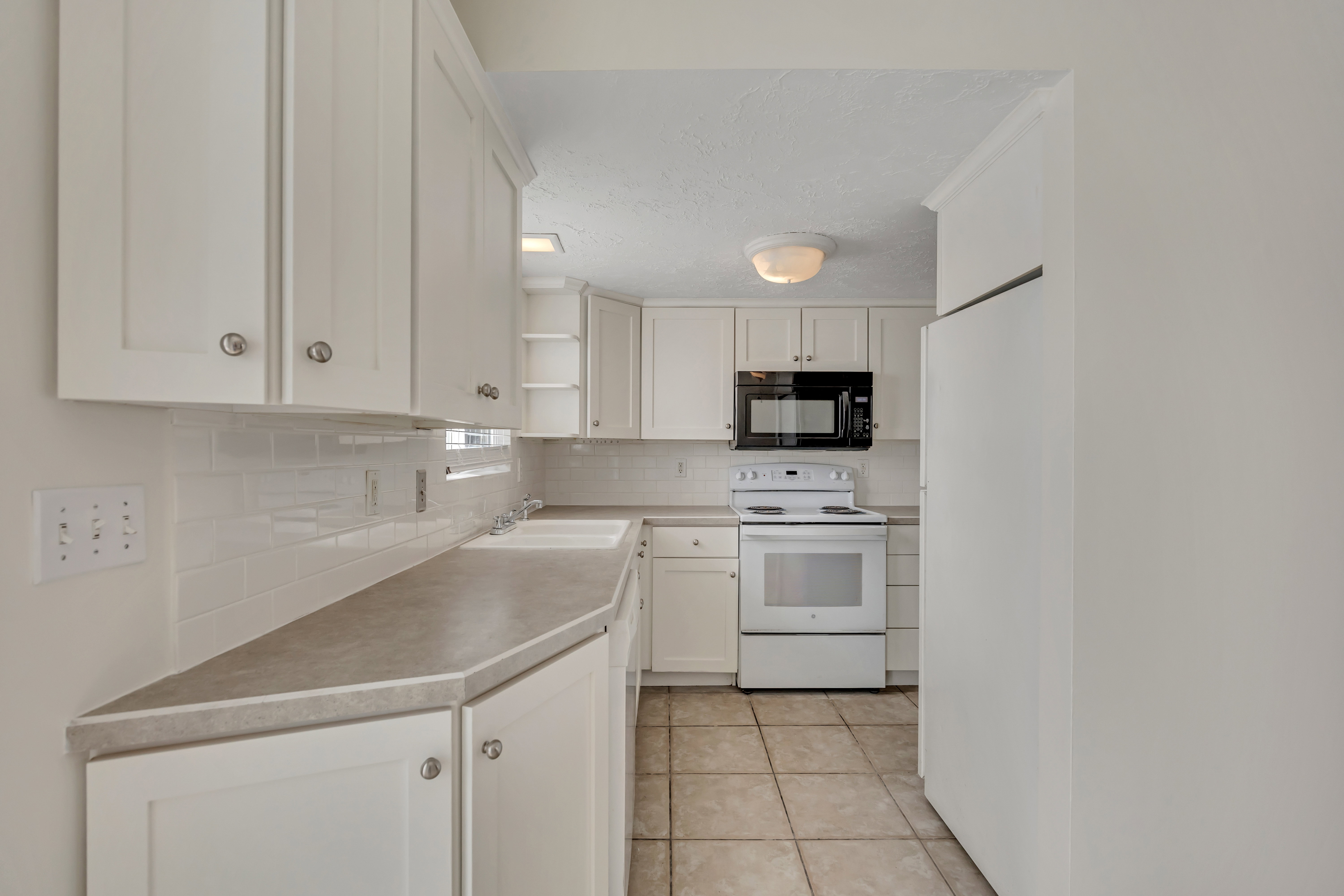 Kitchen with white appliances, white cabinets, open shelves, light tile patterned floors, and decorative backsplash