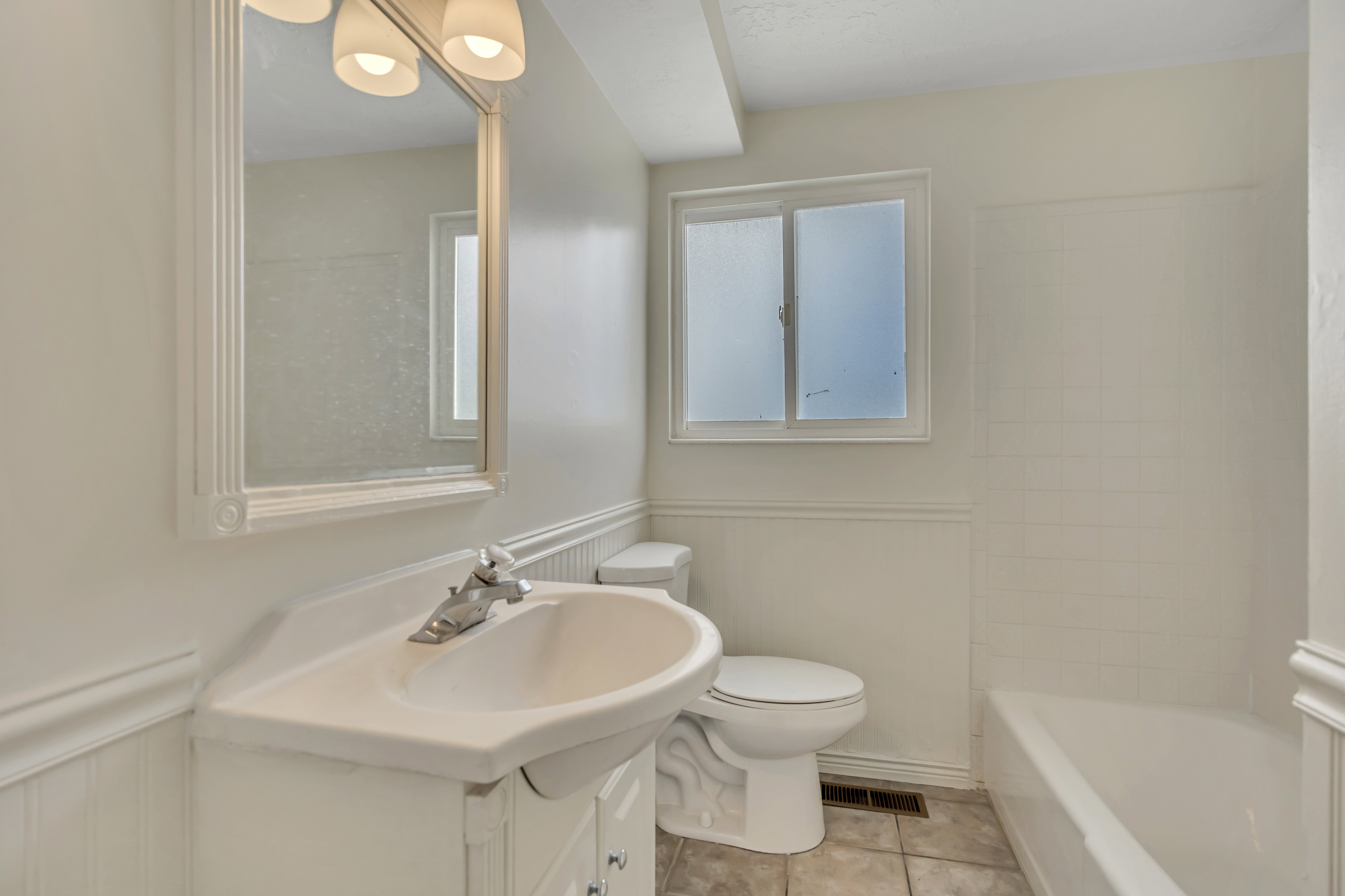 Bathroom featuring a wainscoted wall, vanity, light tile patterned floors, and a decorative wall