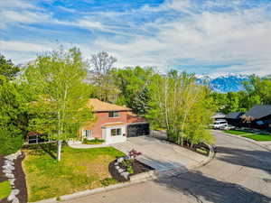View of front of home with brick siding, a mountain view, concrete driveway, and a front lawn