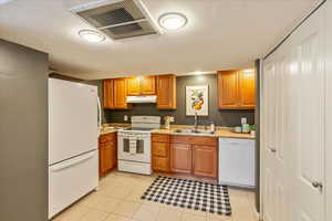 Kitchen with white appliances, light countertops, wood finish cabinetry, and light tile patterned floors