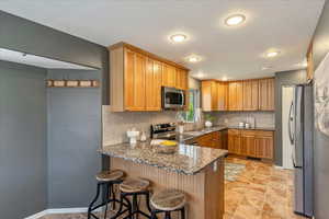 Kitchen featuring dark stone counters, a peninsula, a breakfast bar, and wood finish cabinets