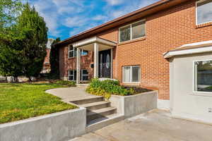 View of exterior entry with a lawn and brick siding