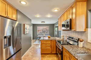 Kitchen featuring stainless steel appliances, a peninsula, light stone countertops, wood finish cabinetry, and recessed lighting