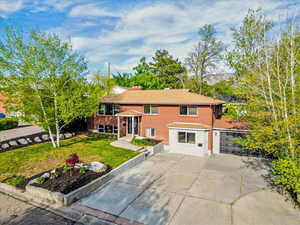 Raised ranch with brick siding, concrete driveway, a front lawn, and a chimney