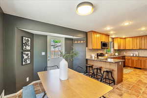Kitchen featuring dark stone countertops, a peninsula, a breakfast bar area, wood finish cabinets, and recessed lighting