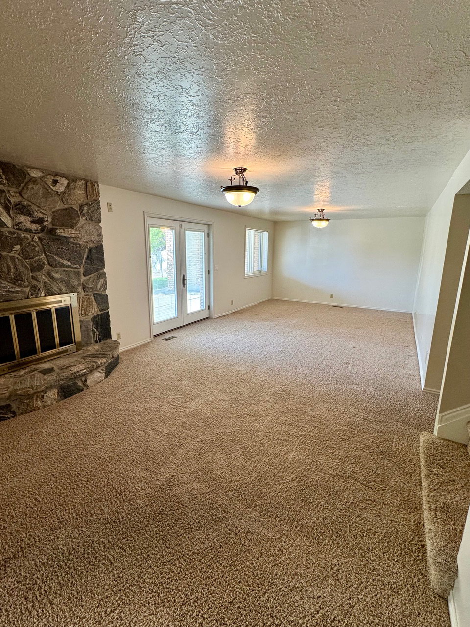 Spacious living area featuring a stone fireplace, light-toned carpeting, and a double-door exterior entry with integrated window blinds
