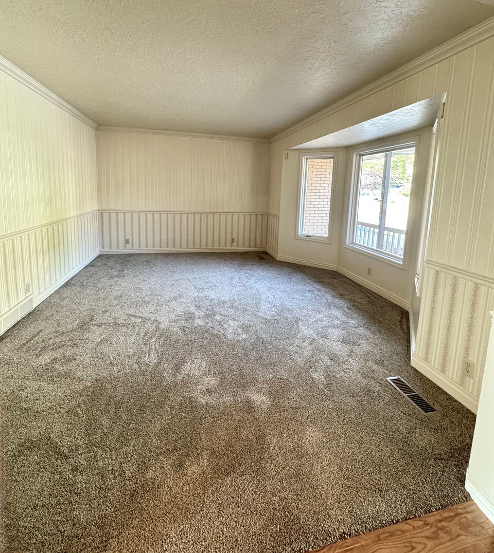 Spacious carpeted room featuring a bay window with brick accents and a decorative wainscoting with striped wallpaper