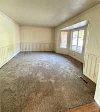 Spacious carpeted room featuring a bay window with brick accents and a decorative wainscoting with striped wallpaper