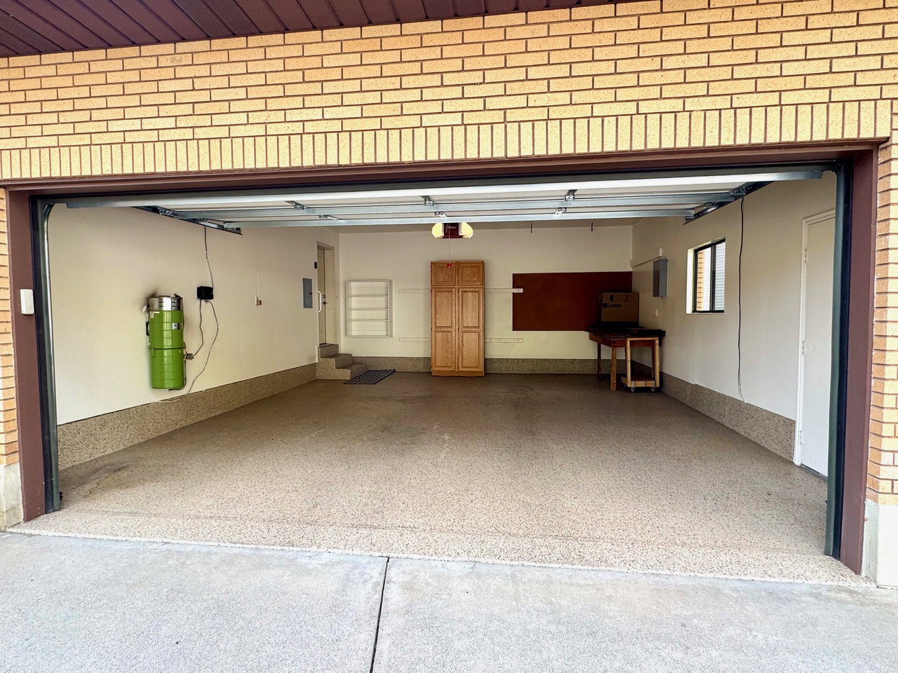 Spacious garage featuring a durable epoxy floor coating, built-in storage cabinetry, transom window, and interior access
