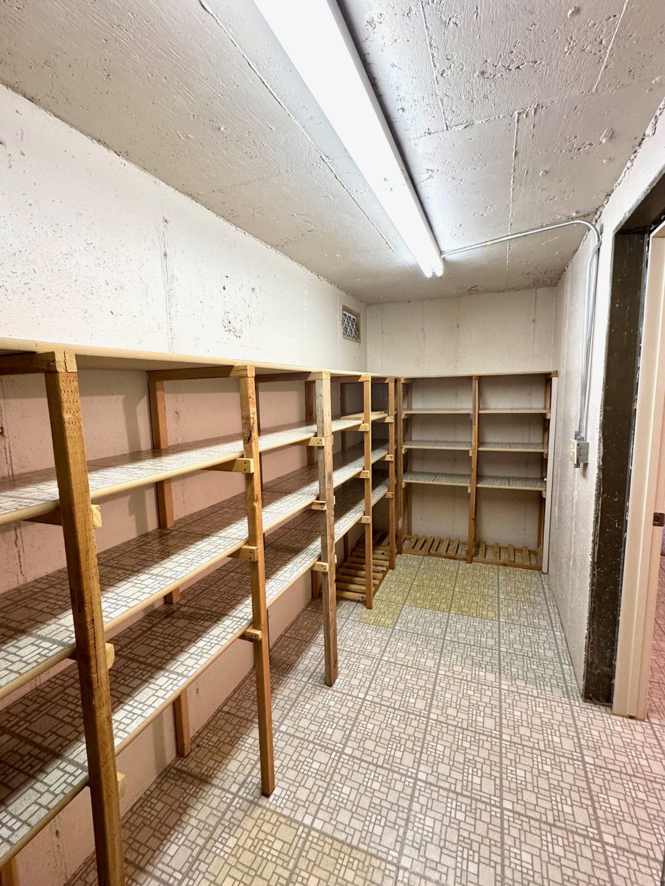 Storage area featuring extensive wood shelving, patterned tile flooring, and overhead fluorescent lighting