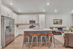 Kitchen with open floor plan, a kitchen breakfast bar, stainless steel appliances, white cabinets, and light wood finished floors