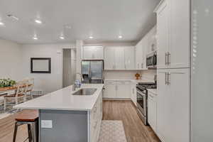 Kitchen featuring stainless steel appliances, a kitchen bar, white cabinetry, light wood-type flooring, and a kitchen island with sink