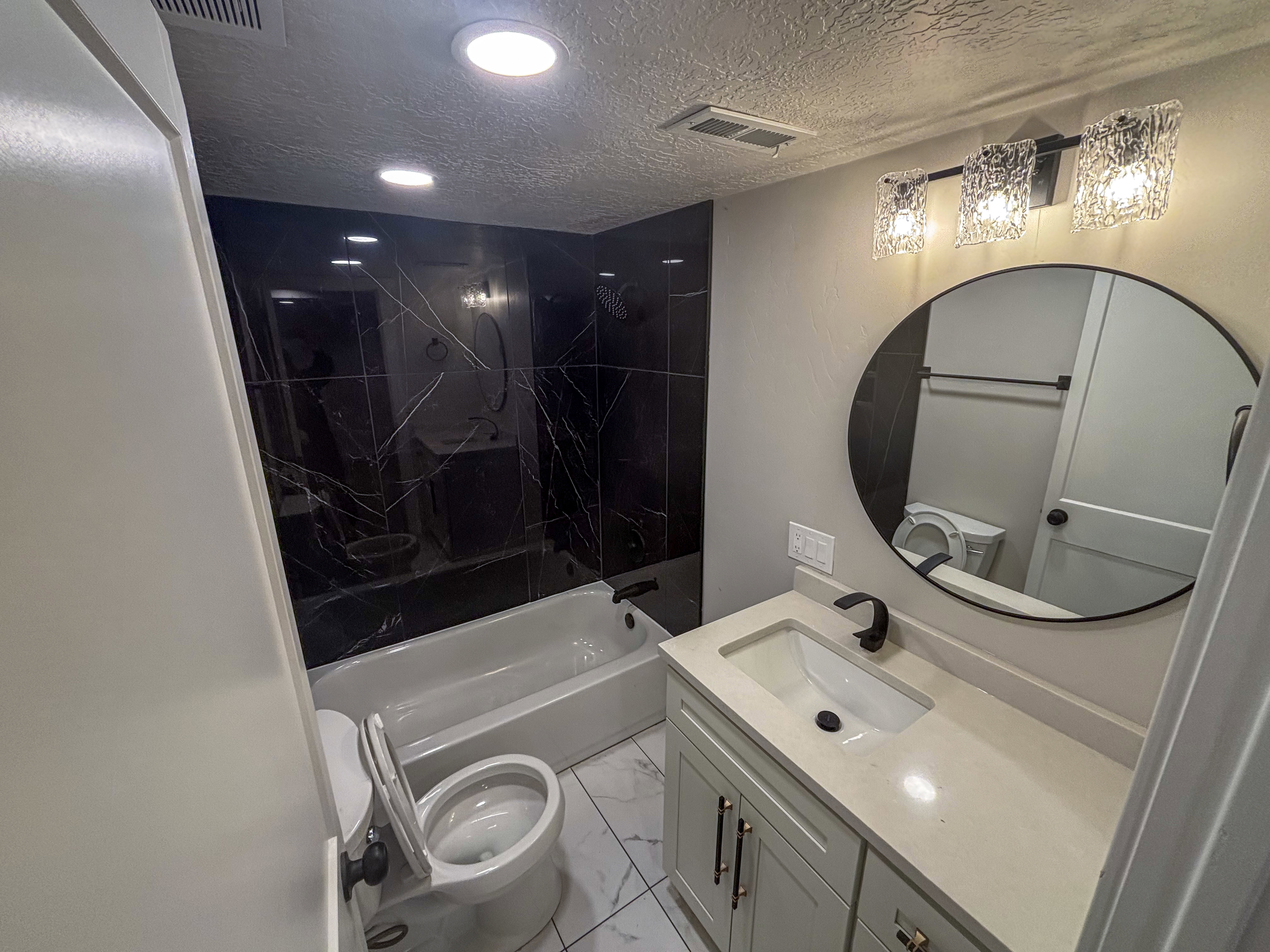Bathroom with vanity, light marble finish flooring, washtub / shower combination, and a textured ceiling