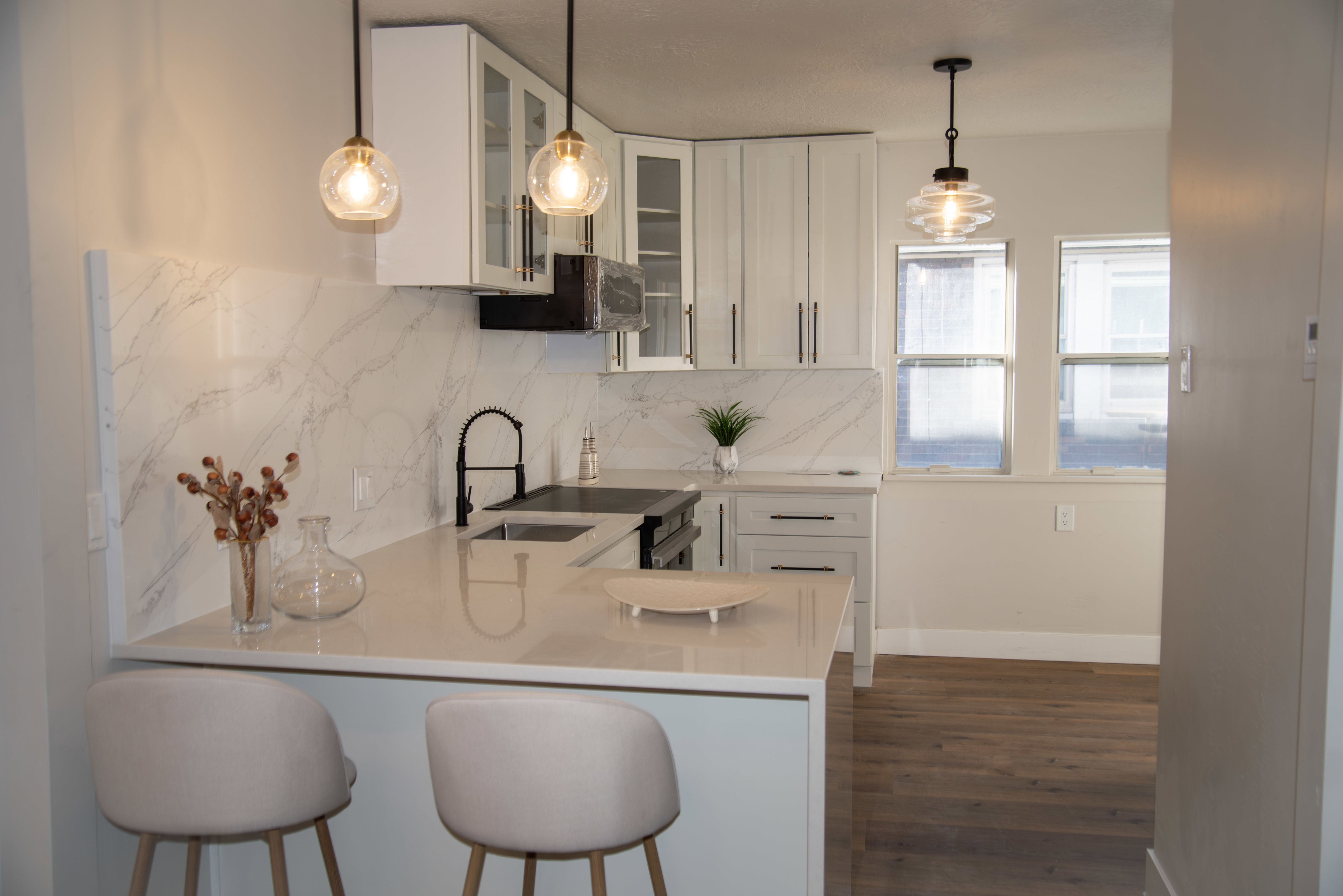 Kitchen featuring white cabinetry, hanging light fixtures, glass insert cabinets, decorative backsplash, and a peninsula
