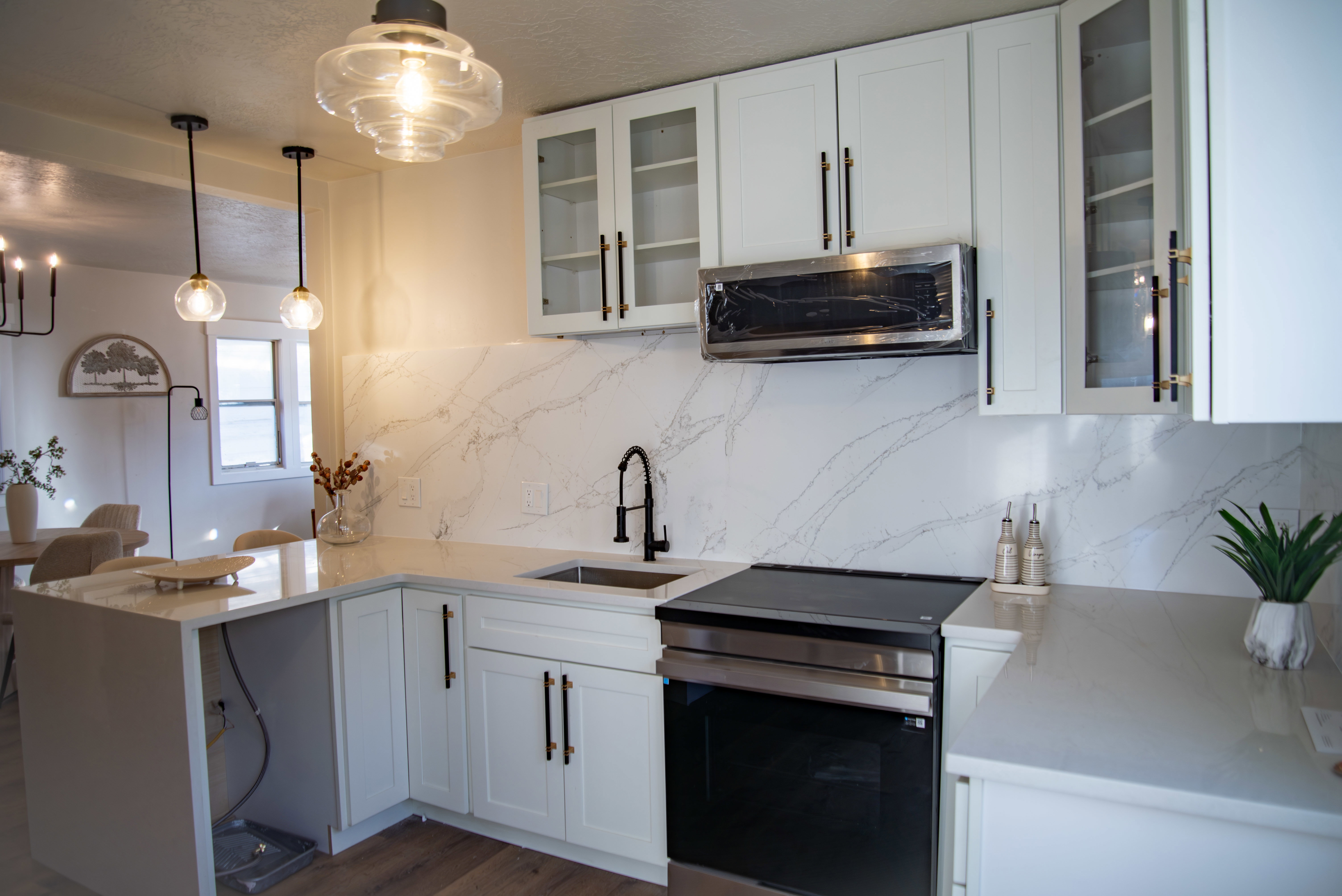 Kitchen with stainless steel appliances, a peninsula, white cabinetry, light stone counters, and hanging light fixtures