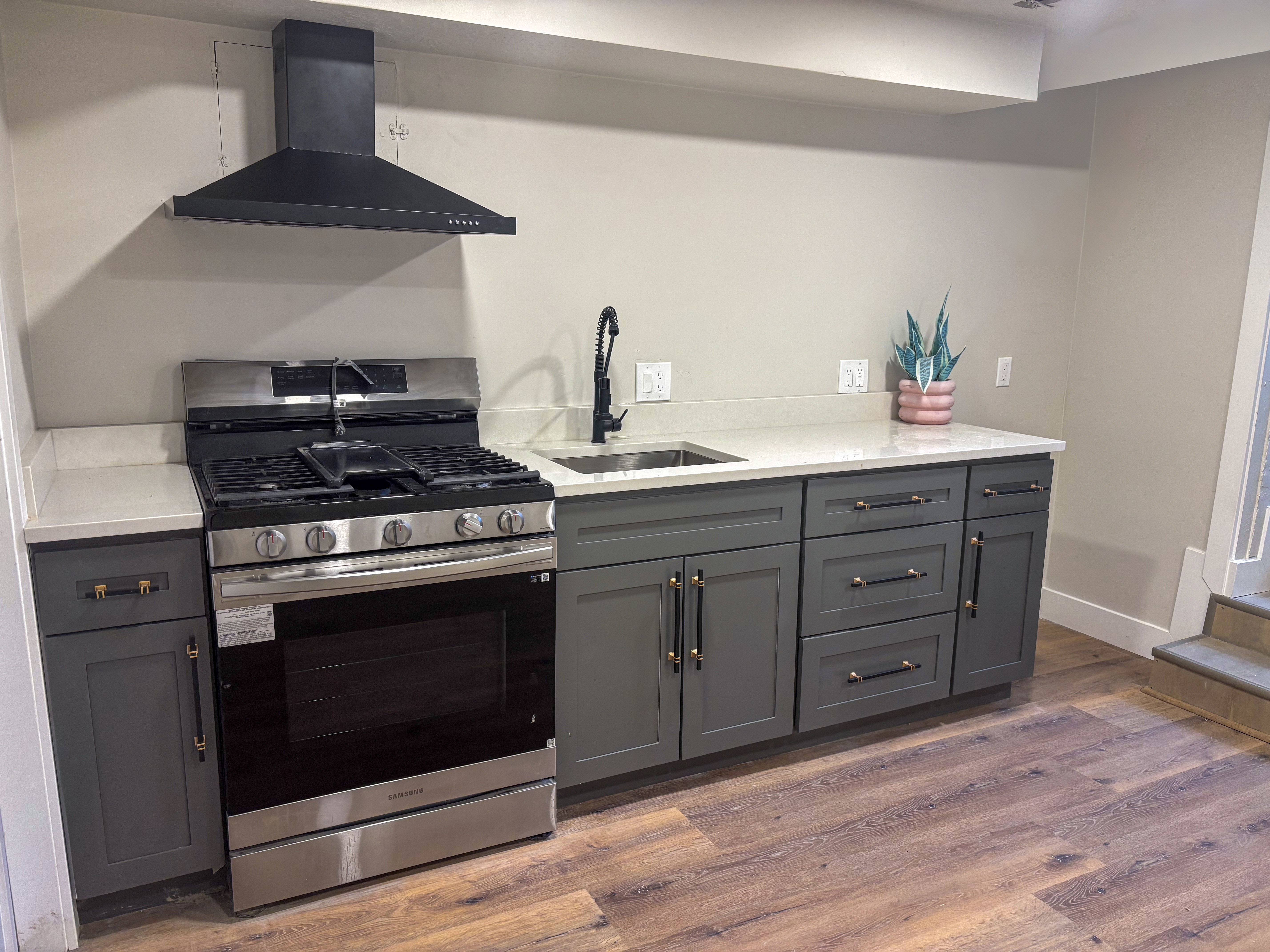 Kitchen featuring stainless steel gas range oven, light stone counters, dark wood-style flooring, and gray cabinets