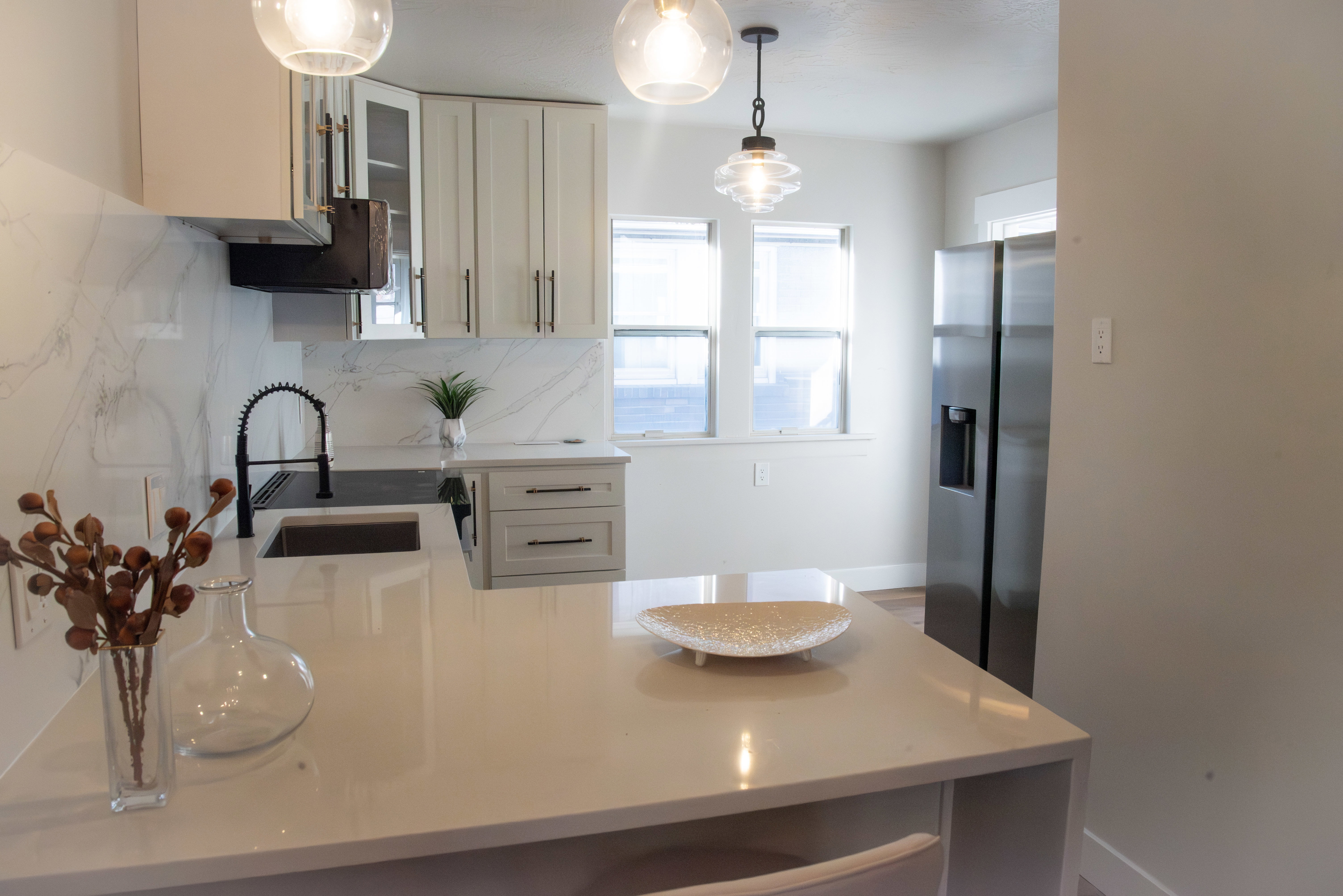 Kitchen with decorative light fixtures, light stone counters, stainless steel refrigerator with ice dispenser, and glass insert cabinets