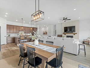 Dining area with light wood-style floors, a warm lit fireplace, ceiling fan, and suspended lighting