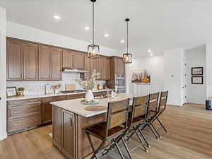 Kitchen with a kitchen bar, pendant lighting, backsplash, a center island with sink, and light wood finished floors