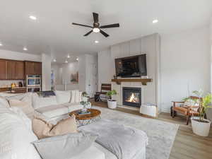 Living area with light wood finished floors, ceiling fan, a glass covered fireplace, and recessed lighting