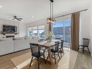 Dining space featuring light wood finished floors, suspended lighting, a fireplace, and ceiling fan