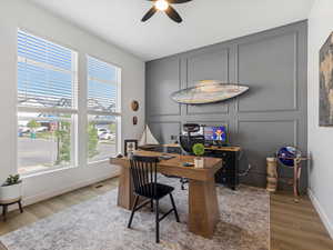 Office space with a decorative wall, ceiling fan, and light wood-style flooring