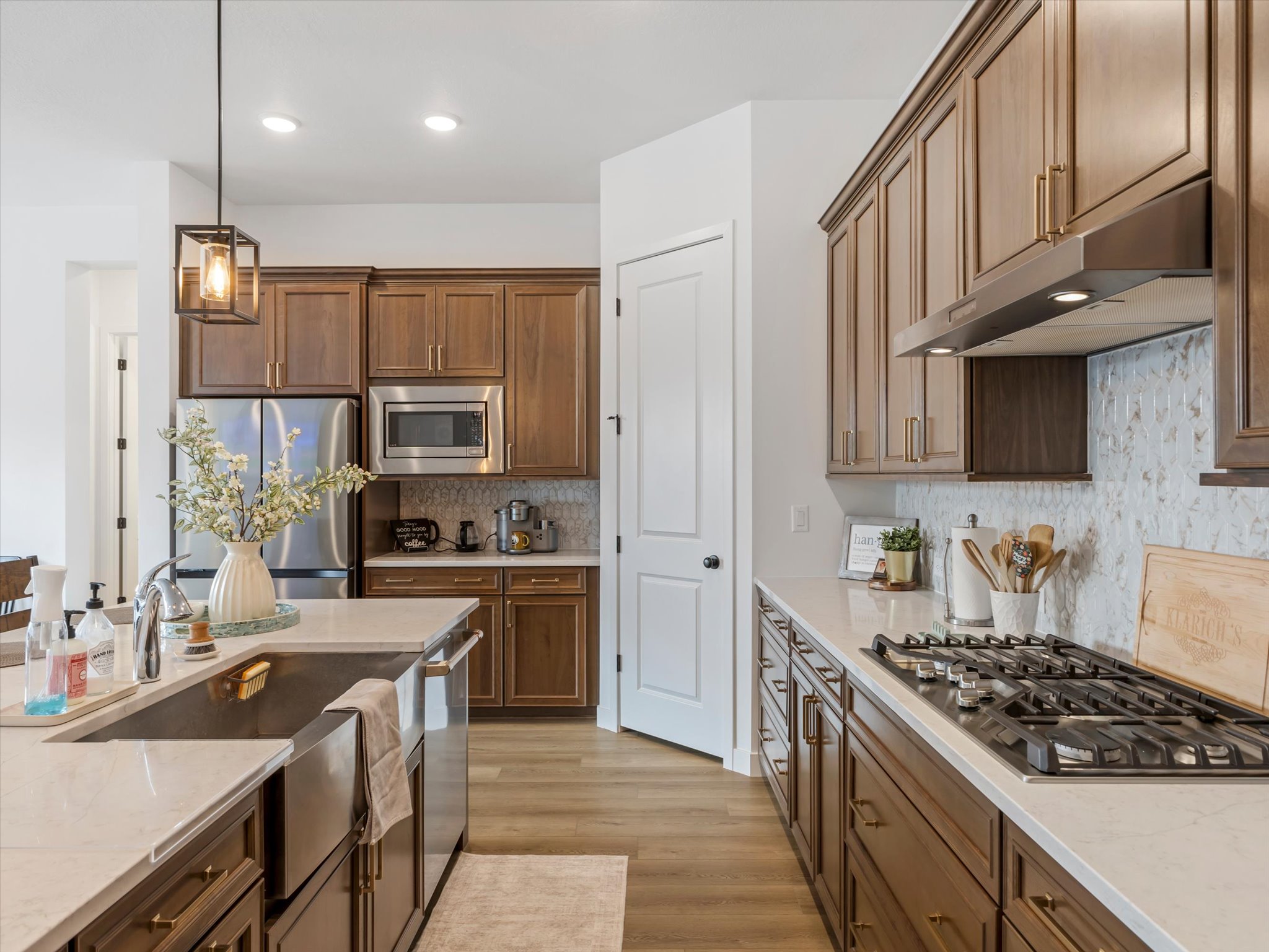 Kitchen featuring stainless steel appliances, pendant lighting, light wood-type flooring, and light stone counters