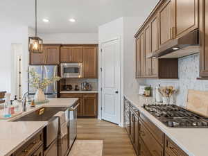 Kitchen featuring stainless steel appliances, pendant lighting, light wood-type flooring, and light stone counters