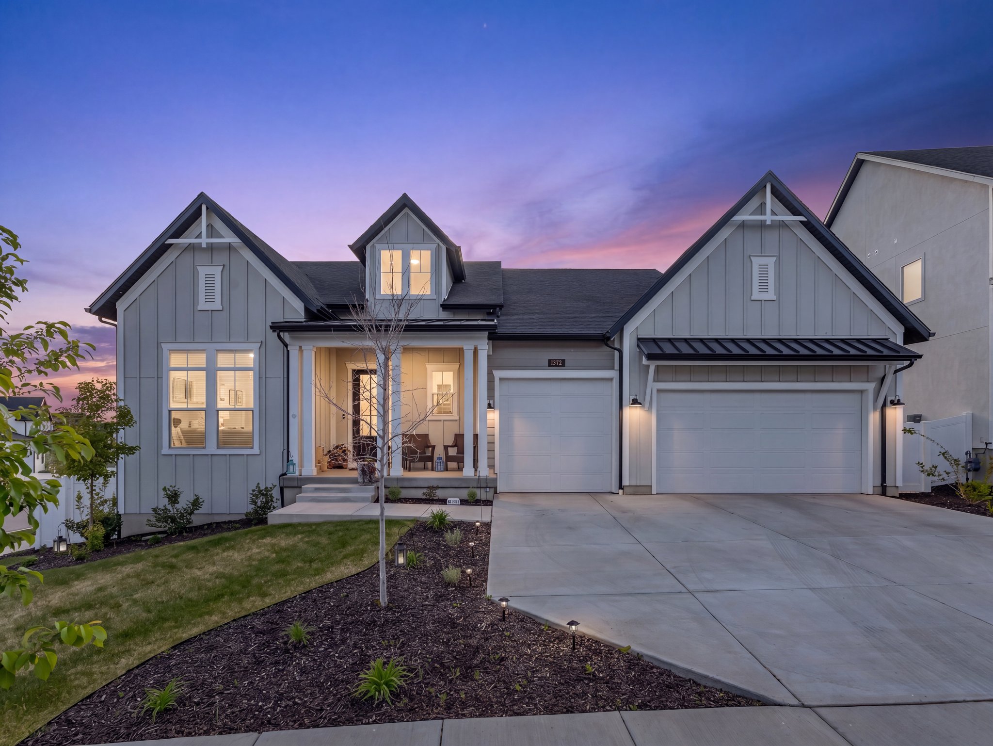 Contemporary craftsman-style residence featuring light gray board and batten siding, dark shingle roof, and a covered porch entry
