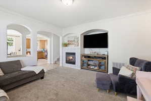 Living area featuring carpet flooring, a tile fireplace, crown molding, and arched walkways