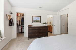 Bedroom with light carpet, a spacious closet, vaulted ceiling, and ensuite bathroom