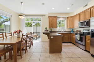 Kitchen featuring stainless steel appliances, light tile patterned floors, pendant lighting, a peninsula, and wood finish cabinetry