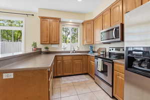 Kitchen with stainless steel appliances, light tile patterned flooring, a peninsula, wood finish cabinets, and recessed lighting
