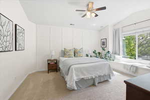 Bedroom with a decorative wall, light colored carpet, ceiling fan, and vaulted ceiling