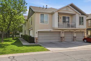 View of front of property with a balcony, stone siding, an attached garage, and stucco siding