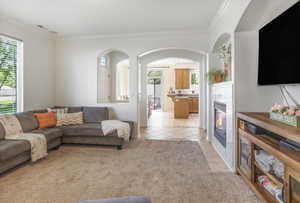 Living room featuring light tile patterned floors, crown molding, a fireplace, arched walkways, and light colored carpet