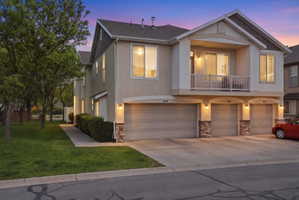 View of front of home featuring stone siding, a balcony, a garage, and stucco siding