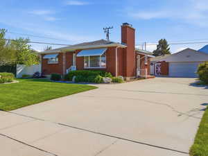 Ranch-style home featuring an outbuilding, a garage, brick siding, a front lawn, and a chimney