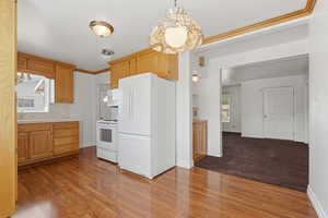 Kitchen featuring white appliances, ornamental molding, light wood finished floors, tile counters, and pendant lighting