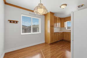 Kitchen with freestanding refrigerator, light countertops, light wood-type flooring, ornamental molding, and hanging light fixtures