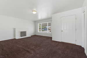 Unfurnished living room featuring dark colored carpet and a brick fireplace