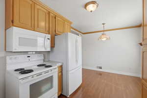 Kitchen featuring white appliances, light countertops, ornamental molding, dark wood-style flooring, and decorative light fixtures