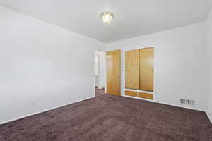 Unfurnished bedroom featuring dark colored carpet and a closet
