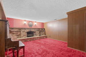 Carpeted living area featuring a brick fireplace, a textured ceiling, and wood walls