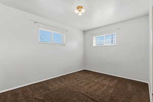 Spare room featuring dark carpet and baseboards