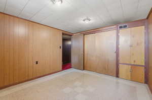 Unfurnished bedroom featuring light flooring, a closet, and wood walls