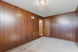 Unfurnished room with a textured ceiling, light carpet, and wooden walls